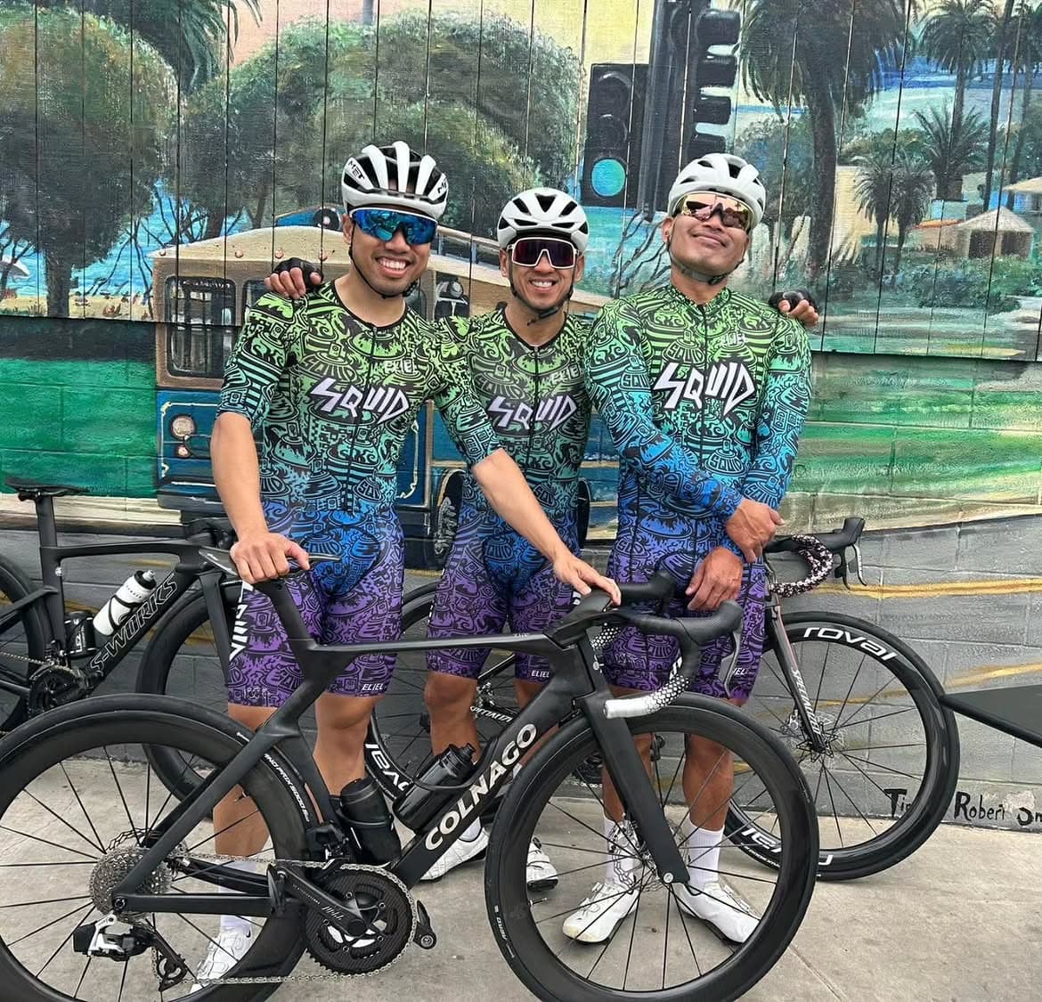 Three cyclists wearing illustrated Squid kits beside their bicycles