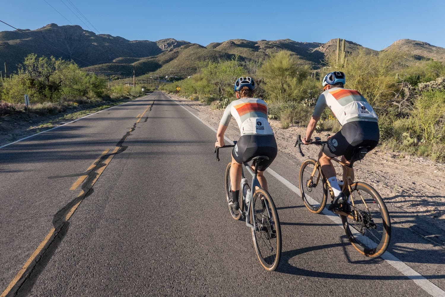 Two cyclists riding through the desert in matching Cycling House kits