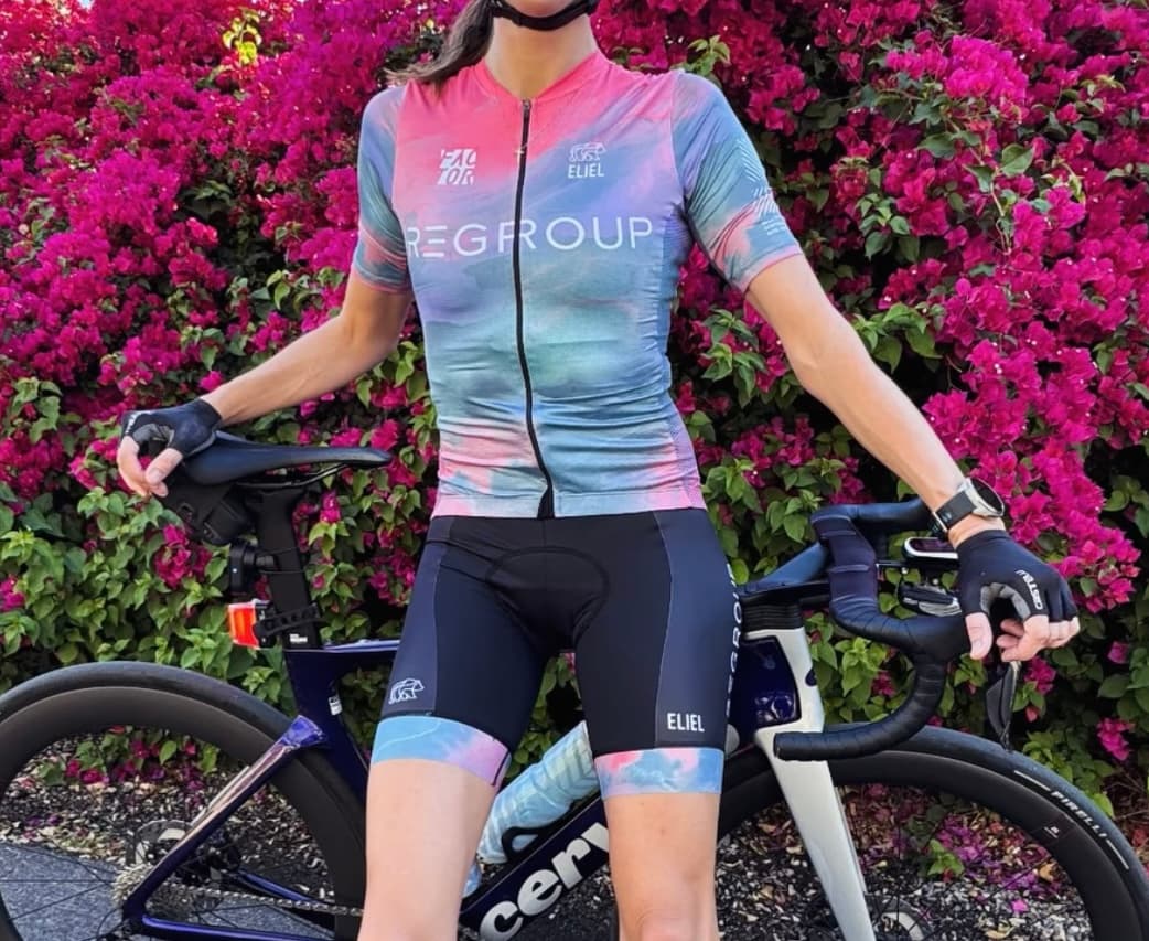 Regroup cycling kit in pink, lilac, and blue, worn beside a road bicycle